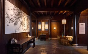 Amanfayun exhibition main hall with dark walls displaying artwork, wooden ceiling beams, and warm ambient lighting.