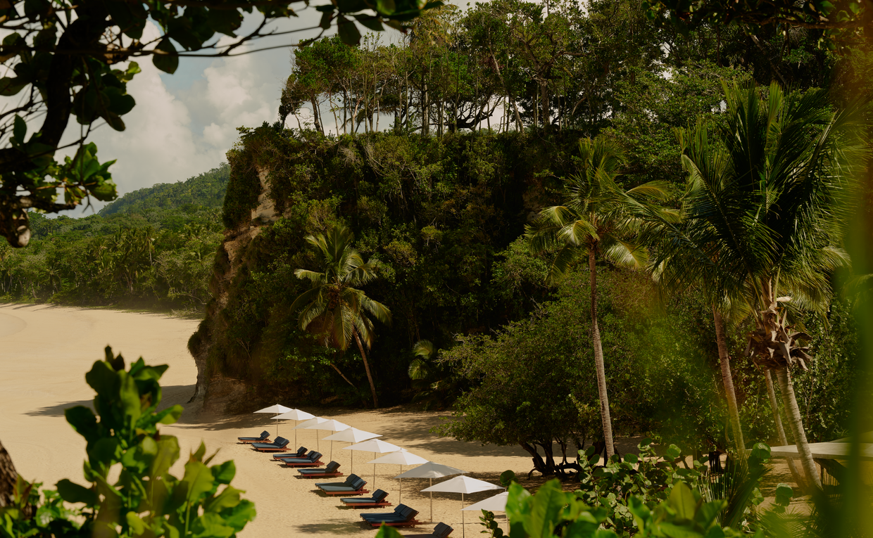 Amanera's beach club terrace with loungers overlooking a sandy cove and tropical vegetation.