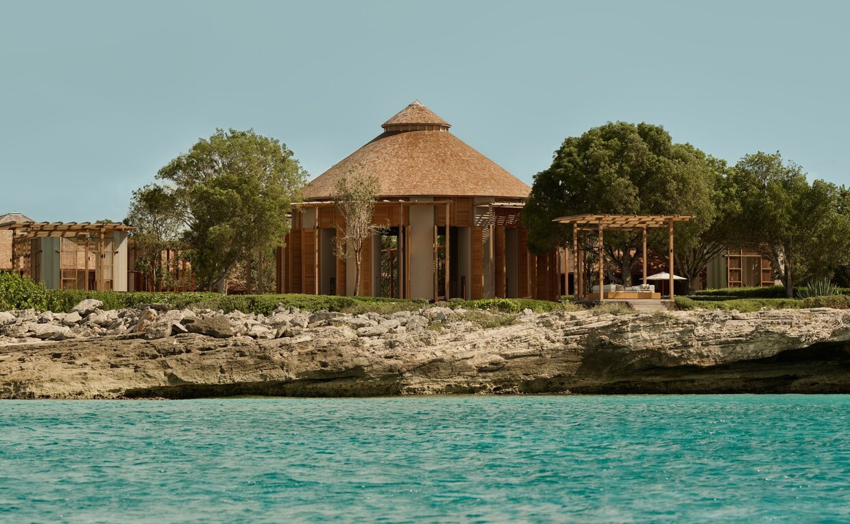 Amanyara's bar pavilion viewed from the water, with turquoise sea and tropical greenery beyond.