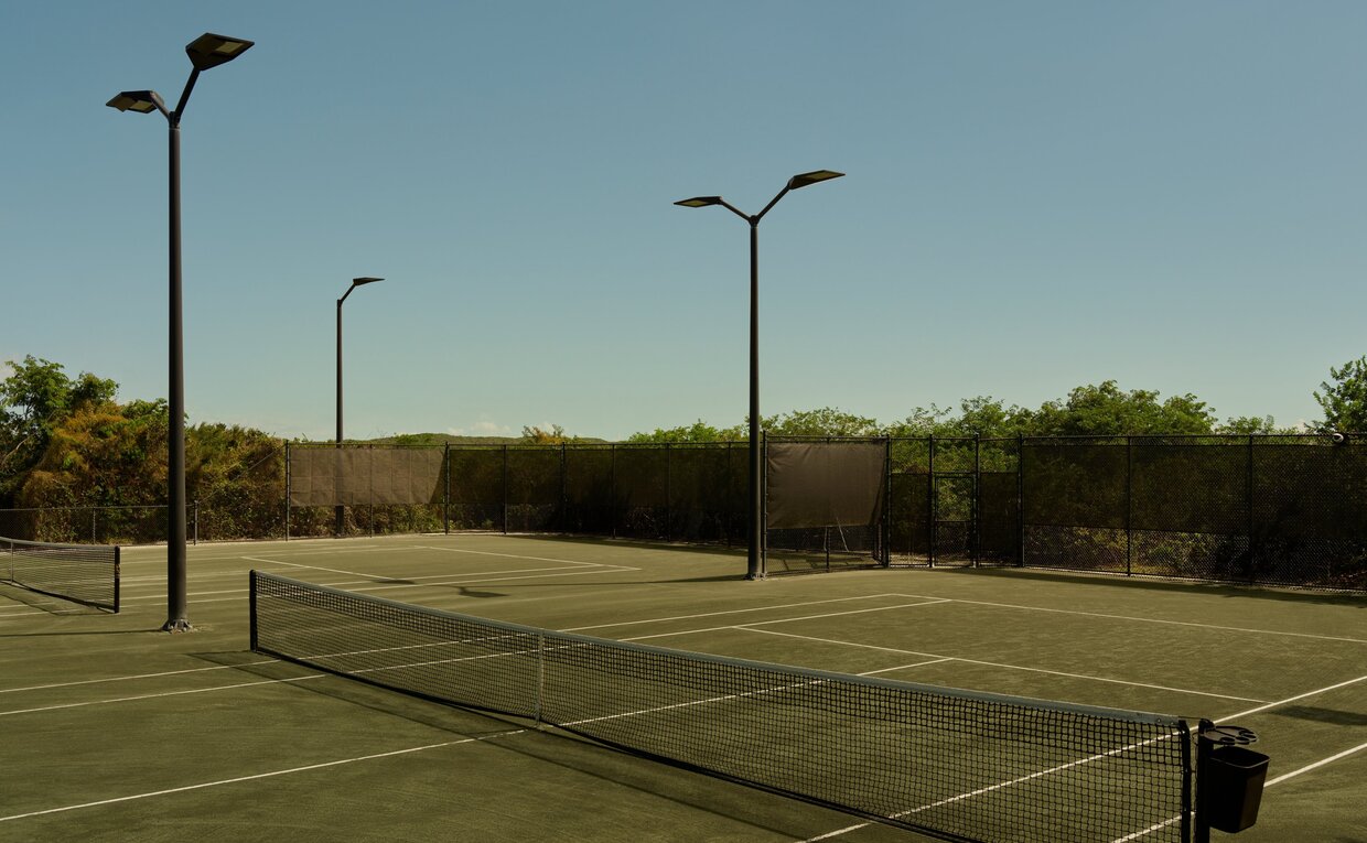 Tennis court at Amanyara with floodlights and surrounding vegetation at dusk.