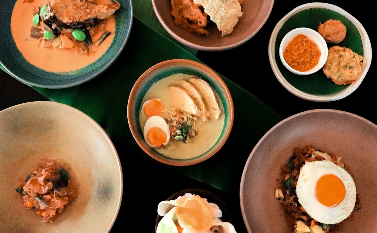 Indonesian dishes served in the dining room at Amanjiwo, featuring soup, rice, and egg preparations on various coloured bowls and plates.