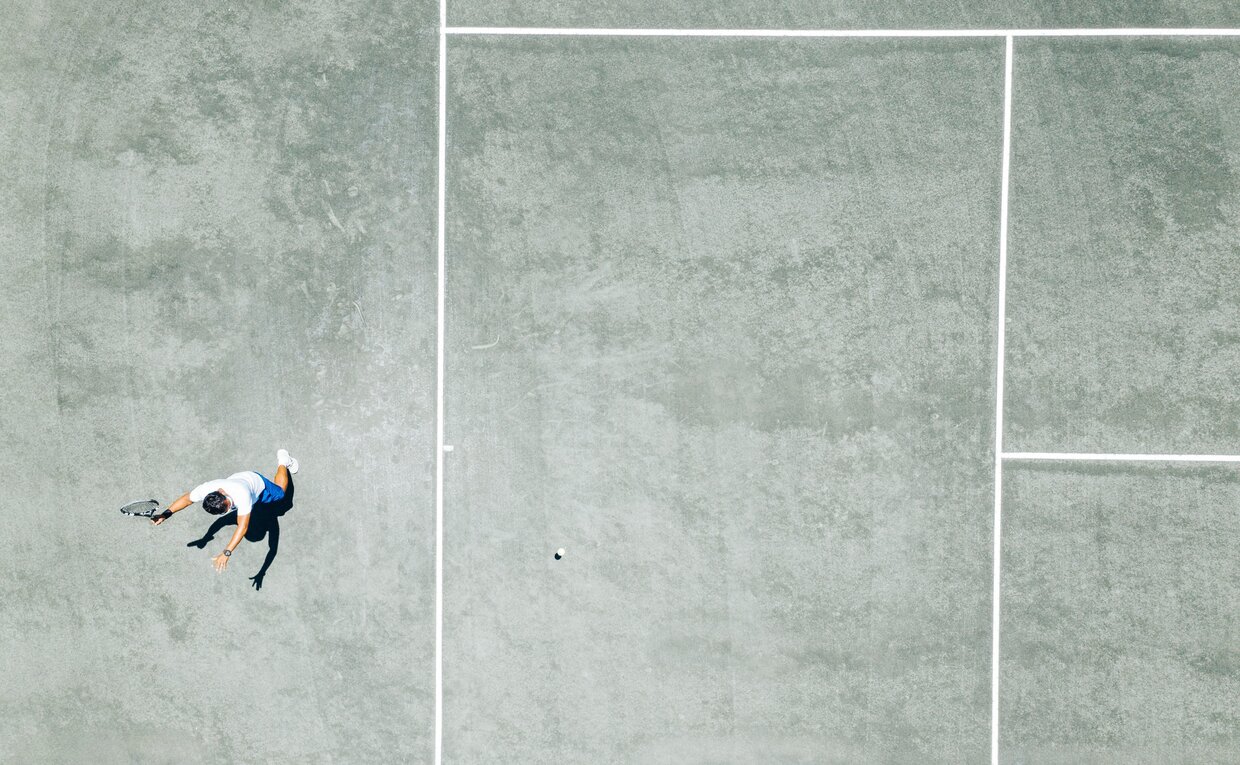 Aerial view of tennis court at Amanyara with players on pale grey surface.