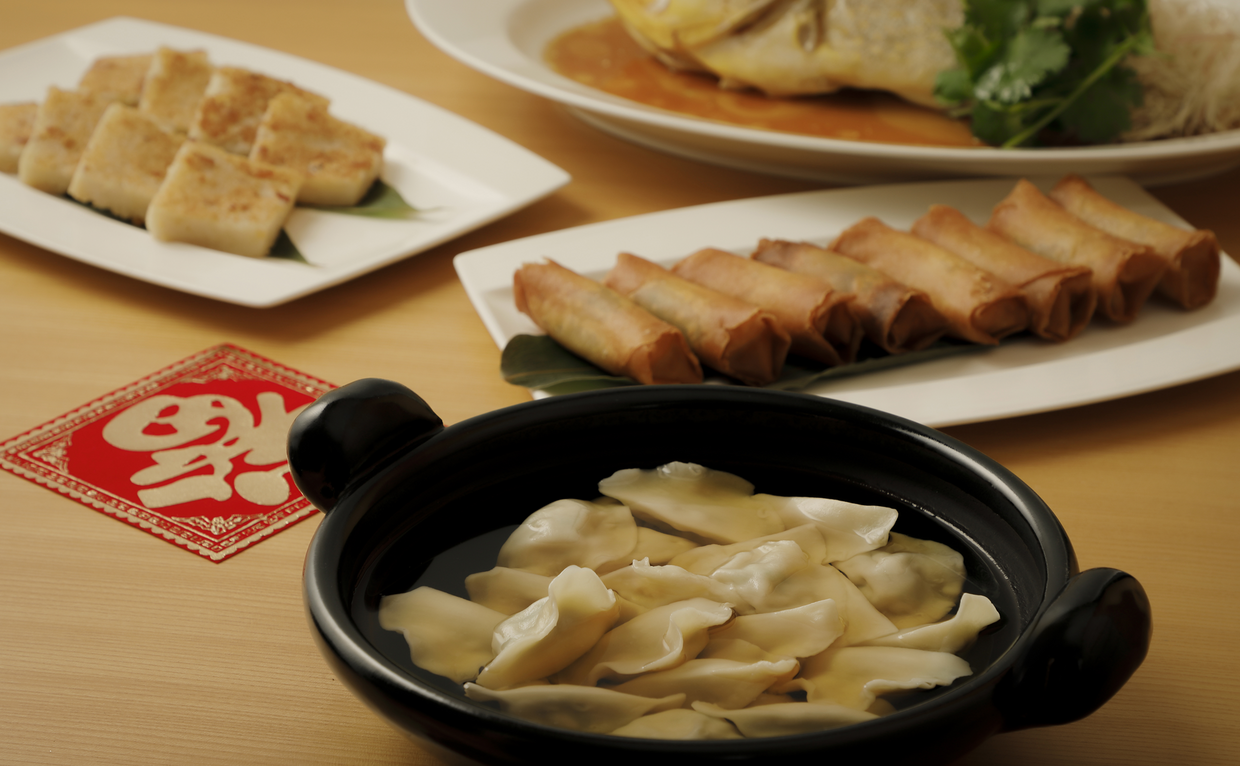 Aman Tokyo lounge dumplings served in a black bowl with steamed buns and noodles on beige table.