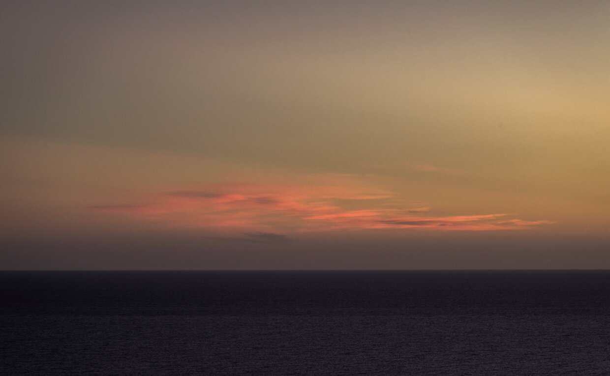 Sunset over the horizon at Amanvari, Mexico, with warm amber and rose tones reflecting across a darkening landscape.