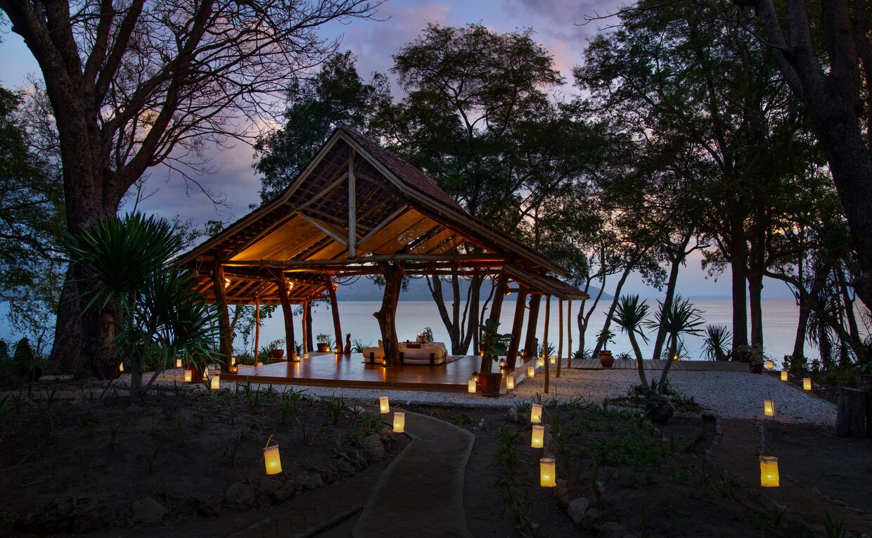Yoga Shala at Amanwana illuminated at dusk, with lanterns lining the open-sided pavilion amongst tall trees.