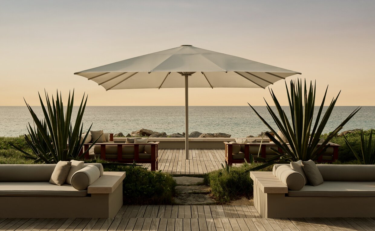 Outdoor terrace at Amanyara with cream parasol, seating area, and tropical plants at sunset.