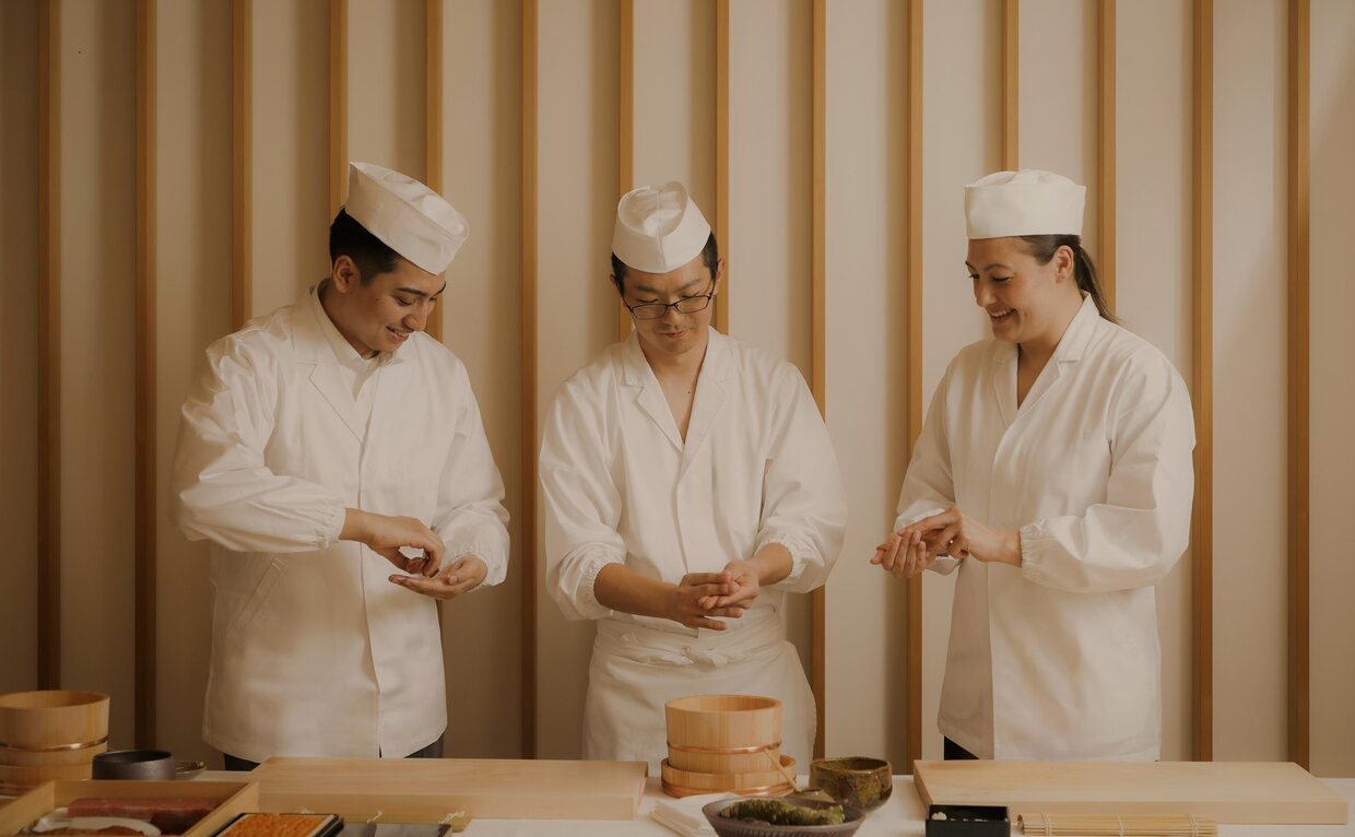 Three chefs in white uniforms and hats prepare sushi during a class at Aman Tokyo, Japan.