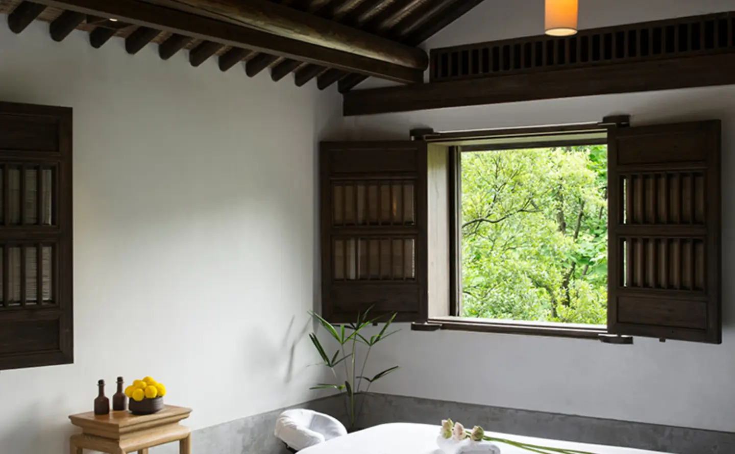 Amanfayun spa treatment room with striped wooden ceiling, pendant lights, and bathtub overlooking garden views.