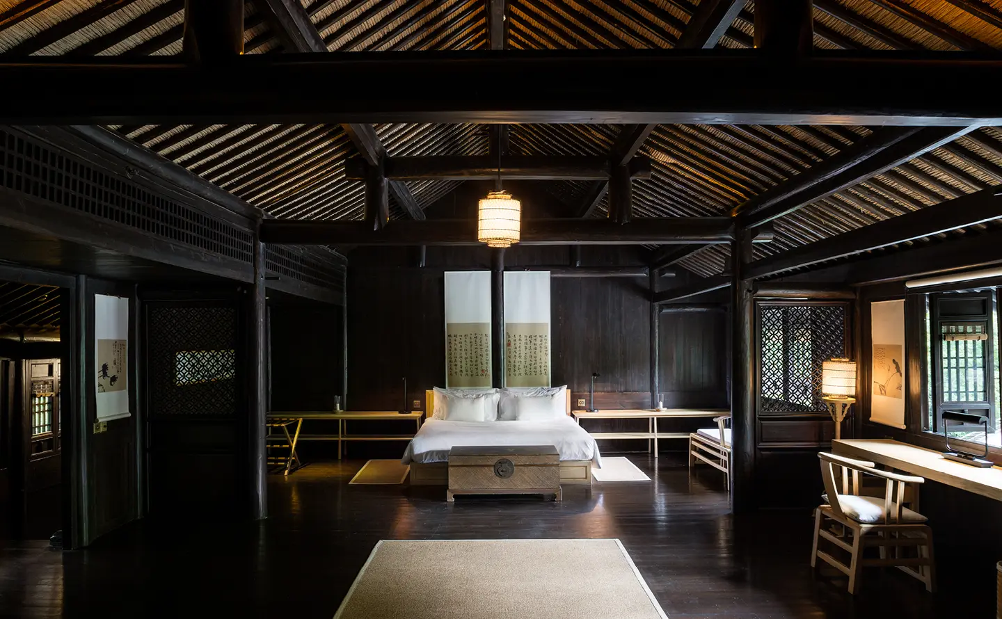 Amanfayun bedroom with dark timber ceiling, central bed, and warm pendant lighting.