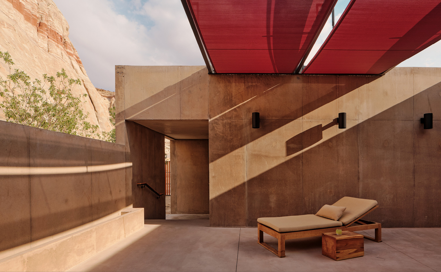 安缦奇岭度假村的露天空间，沙色石墙下置有木制躺椅，红色遮阳篷提供庇荫。