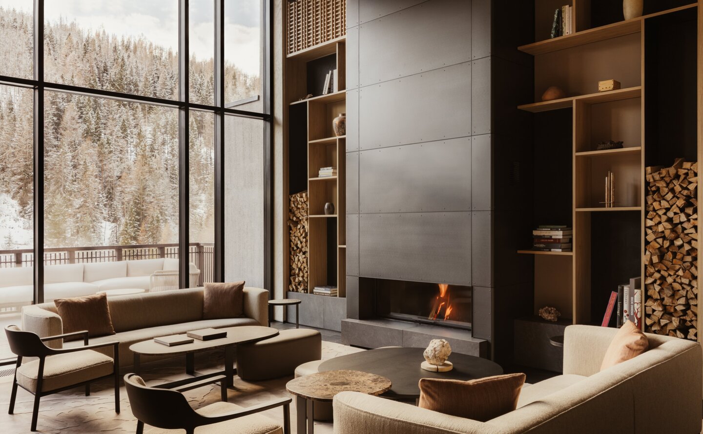 Il Salotto lounge at Aman Rosa Alpina with contemporary seating, fireplace and floor-to-ceiling windows overlooking the Italian Alps.