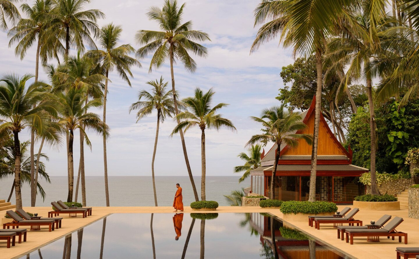 Buddhist monk in saffron robes at Amanpuri's main pool overlooking Thailand's coastal waters, during a blessing ceremony.