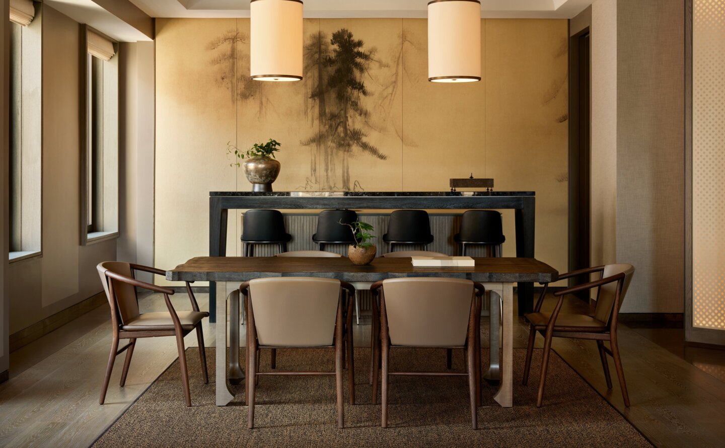 Dining area in an Aman Suite at Aman New York, featuring a wooden table with chairs and pendant lighting.