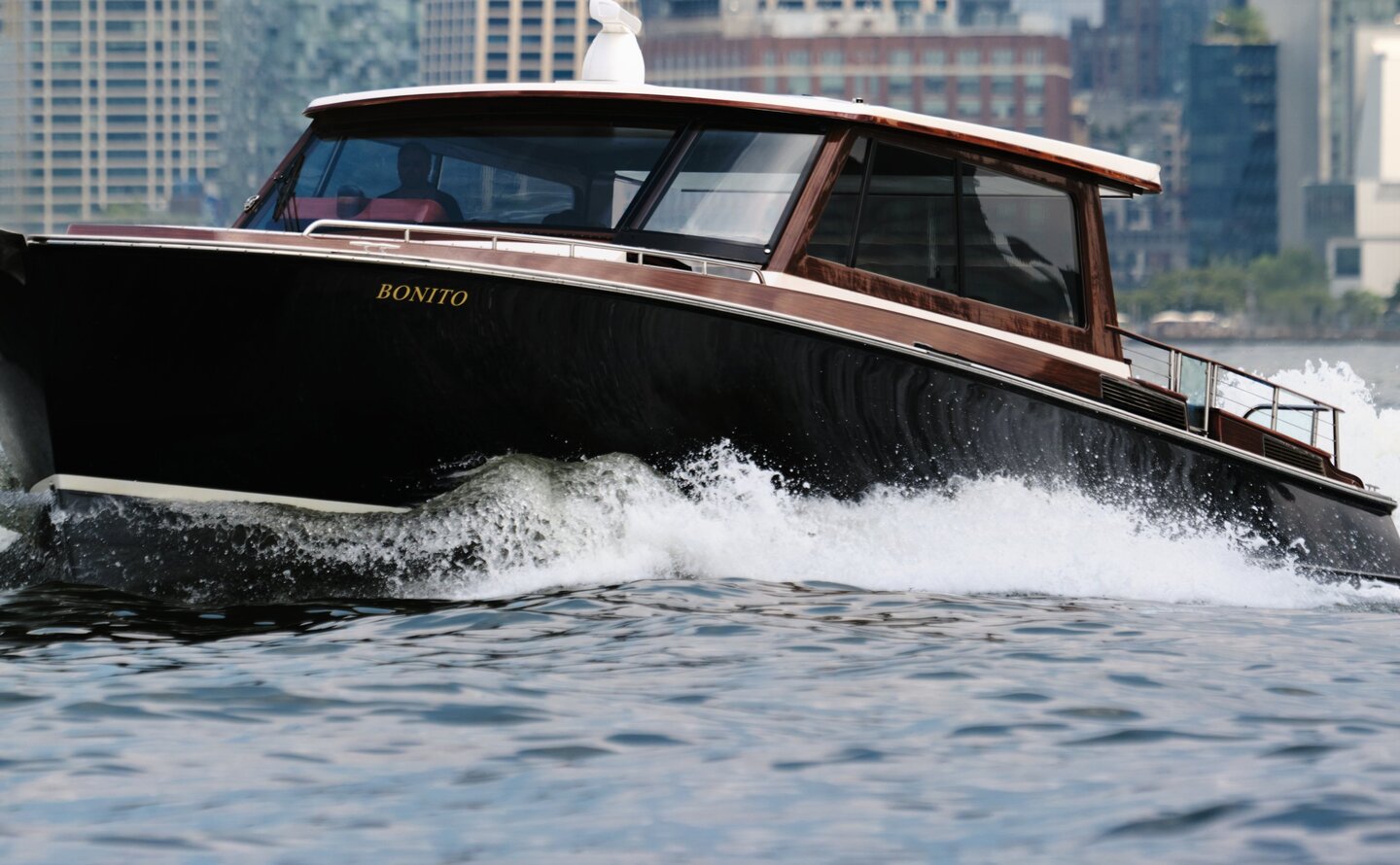 Sleek black speedboat cutting through Hudson River waters with Manhattan skyline behind, Aman New York.