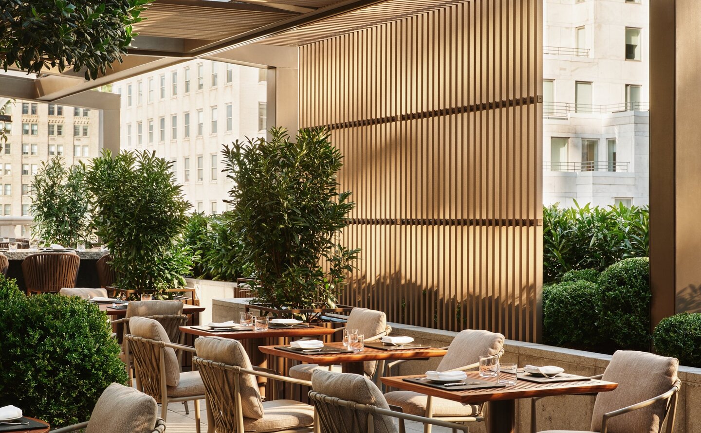 Garden terrace at Aman New York with dining table, chairs, and potted plants beneath a corrugated metal canopy.