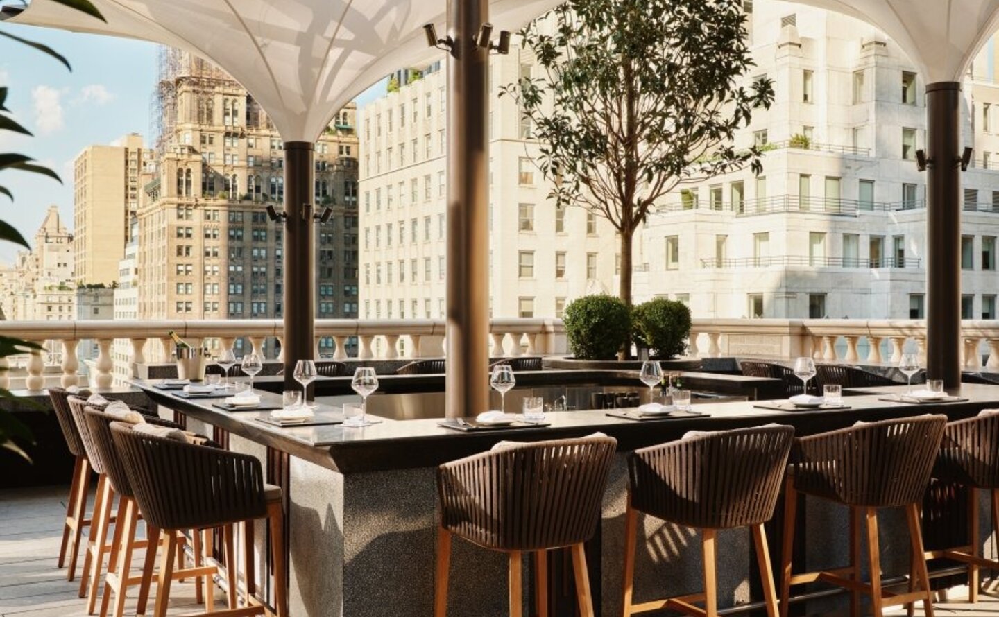 Garden terrace bar at Aman New York with wooden seating and city views.