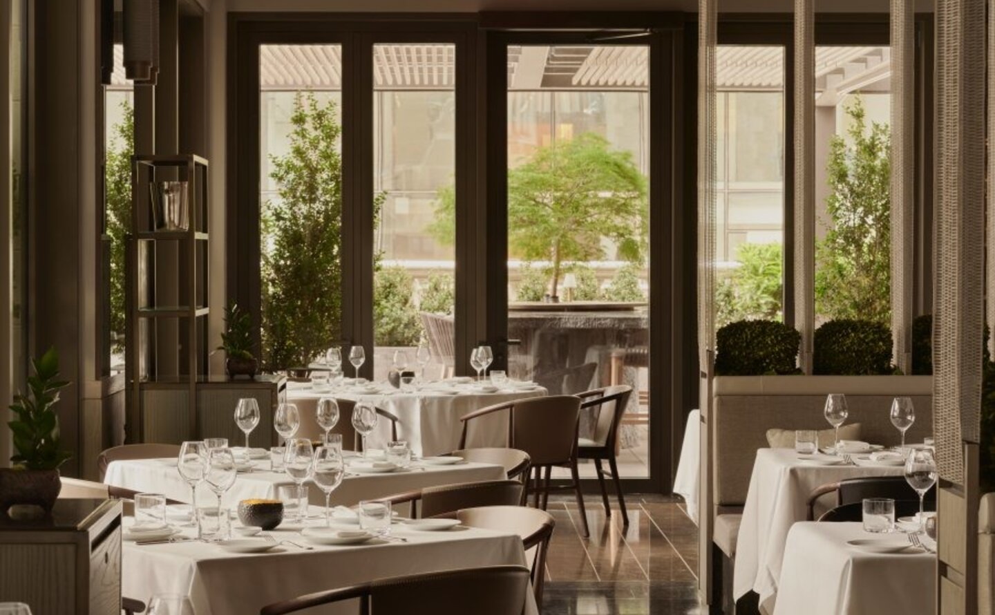Arva dining venue at Aman New York, with table settings overlooking verdant city views through tall windows.