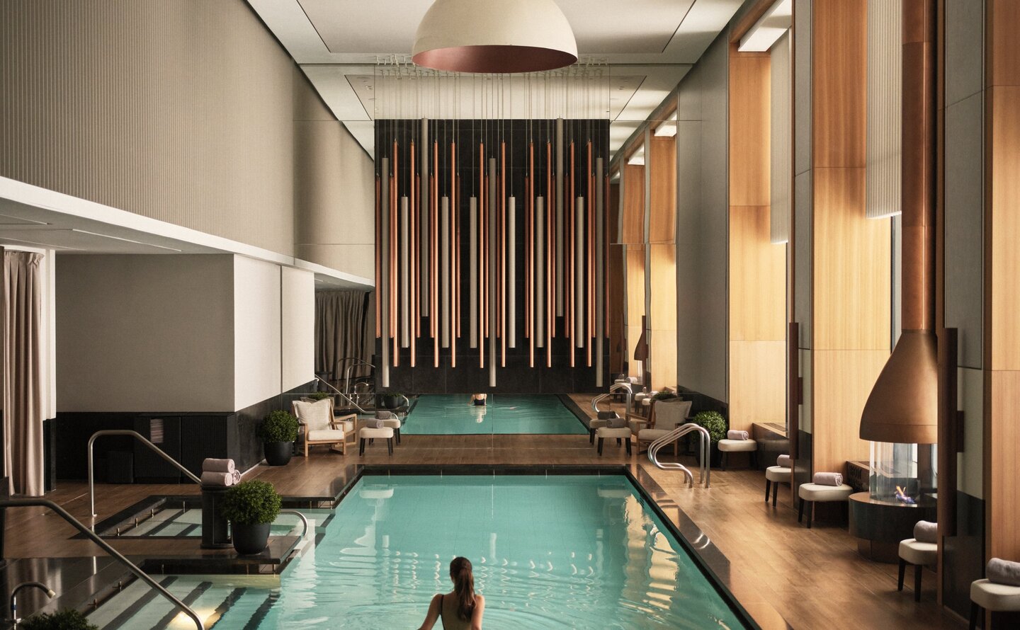 Swimming pool at Aman New York with warm lighting and floor-to-ceiling windows.