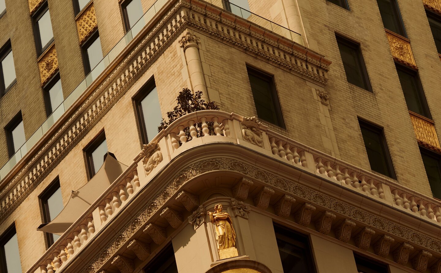 Ornate limestone façade with arched windows at Aman New York, viewed from below against surrounding modern buildings.