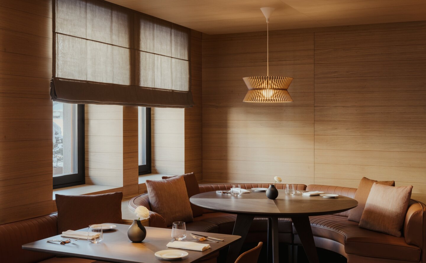 The Grill dining room at Aman Rosa Alpina, featuring wooden interiors, large windows, and an intimate table setting.