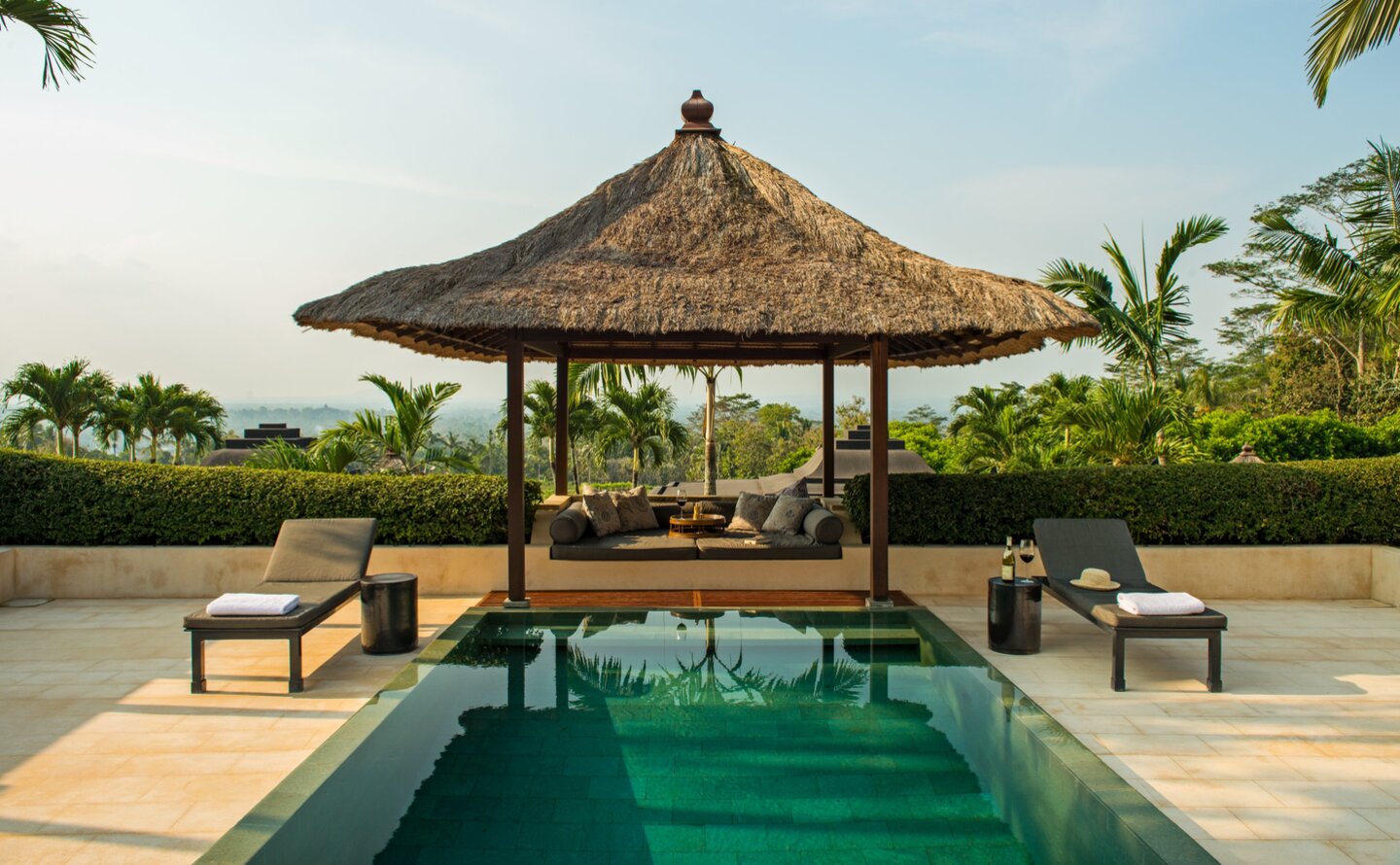 Amanjiwo's pool pavilion overlooks a reflecting pool with traditional pitched roof and wooden loungers.