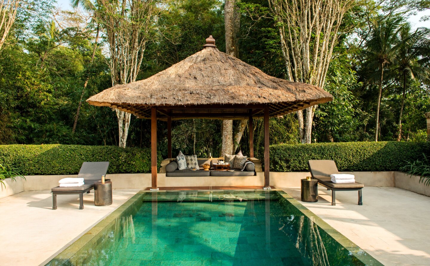 Garden pool pavilion at Amanjiwo with thatched roof, emerald waters, and surrounding greenery in Indonesia.