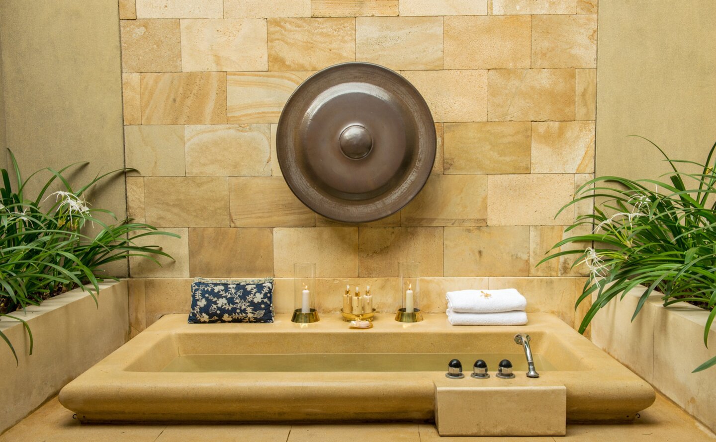 Outdoor bath at Amanjiwo with stone surround, overhead rainfall showerhead, and potted plants on either side.