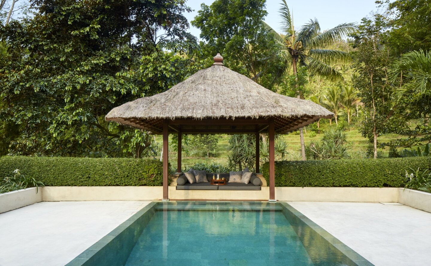 Thatched pavilion overlooking a plunge pool at Amanjiwo, surrounded by lush greenery in Menoreh, Indonesia.