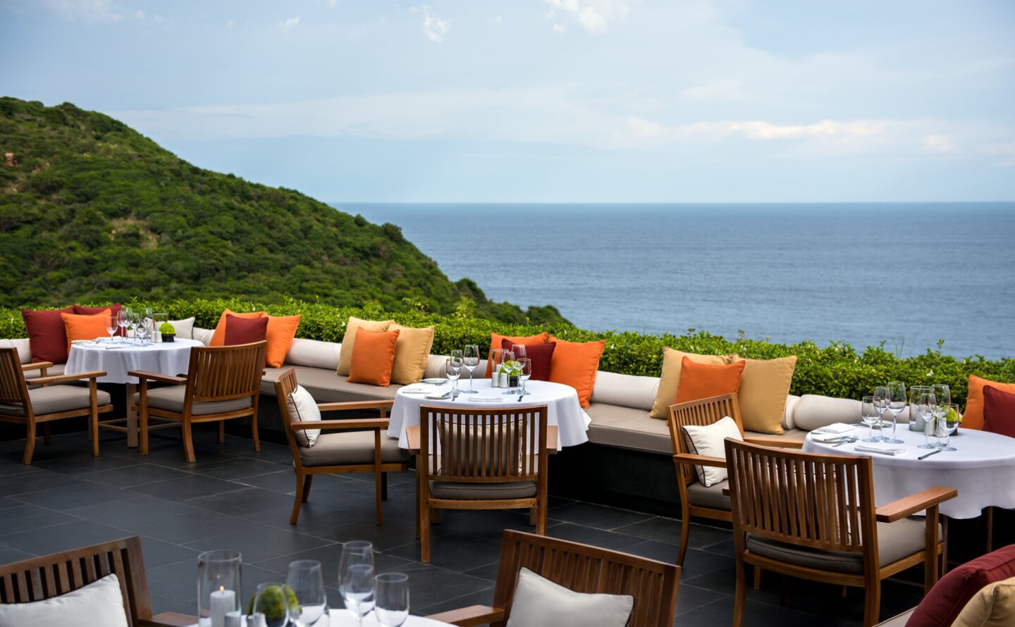Amanoi's main restaurant terrace with colourful cushioned seating overlooking coastal hills and sea.
