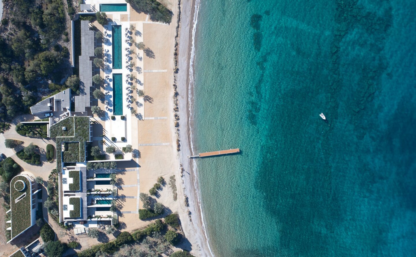 Aerial view of Amanzoe's beach club with sandy shore, turquoise waters and coastal architecture.