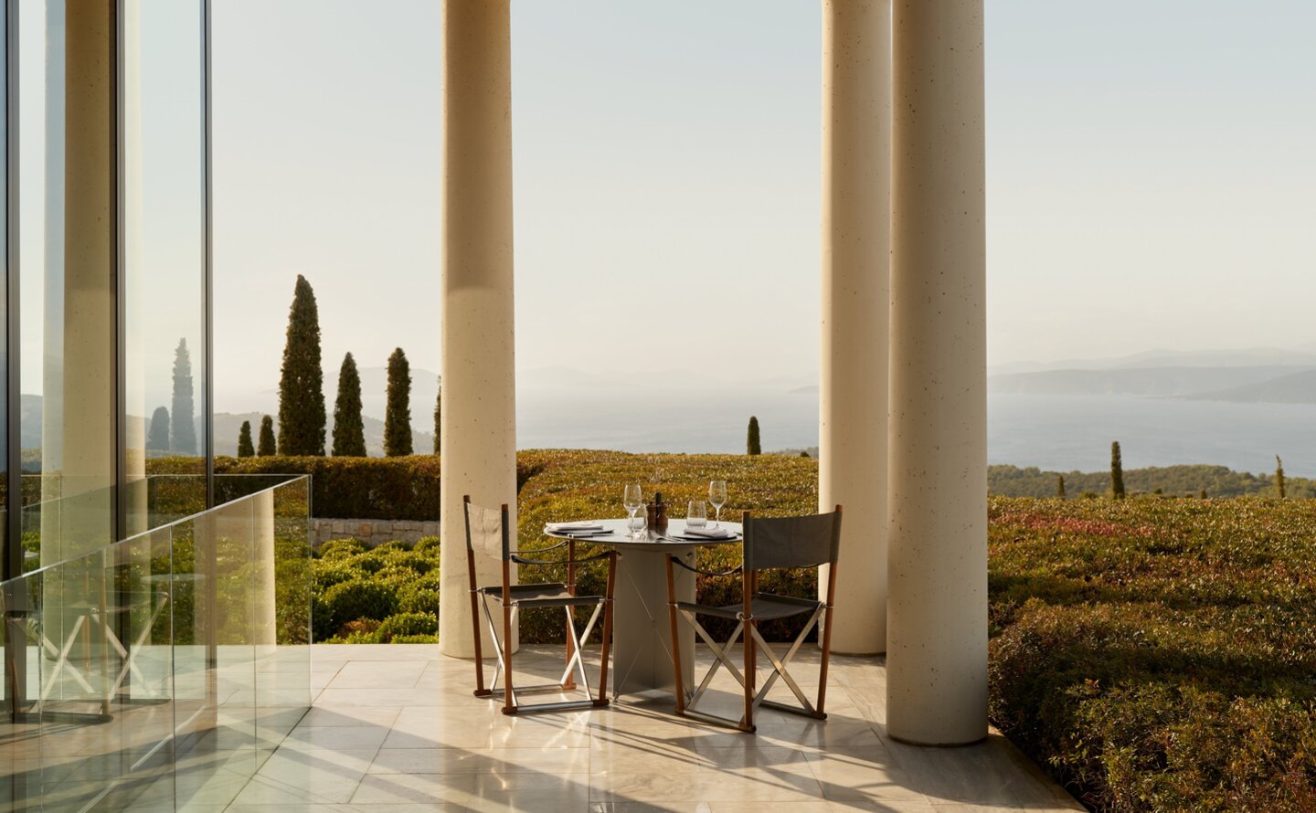 Dining area at Amanzoe's main restaurant with floor-to-ceiling windows overlooking the Greek coastline.