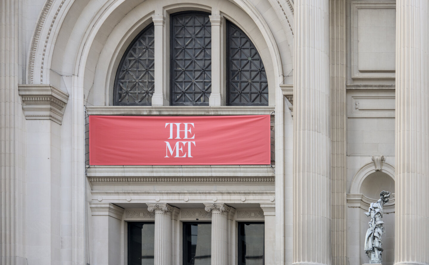 Red entrance canopy beneath an arched doorway at Aman New York.
