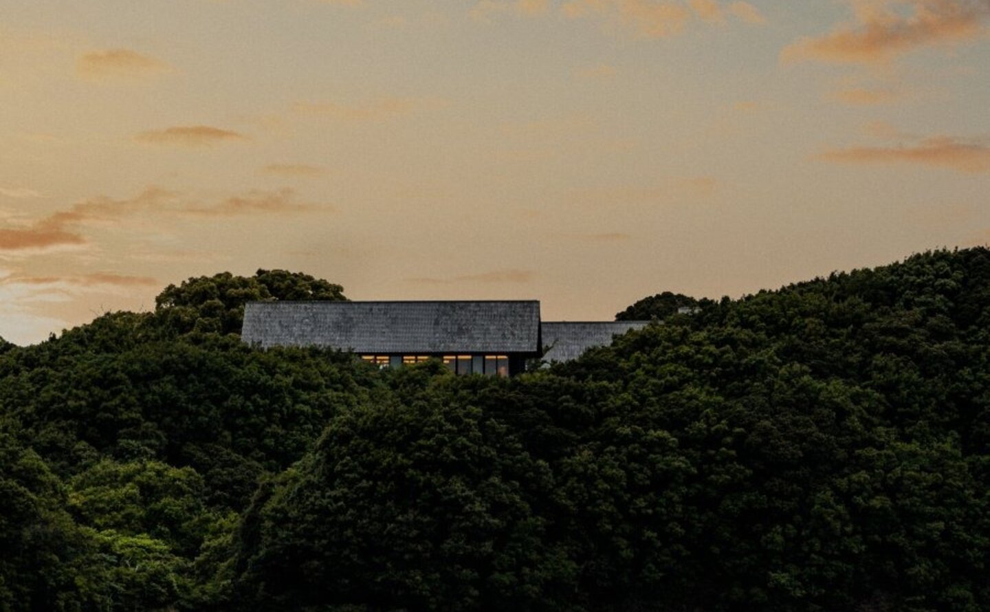 Amanemu's modern architecture positioned on a forested hillside at sunset, overlooking calm waters.