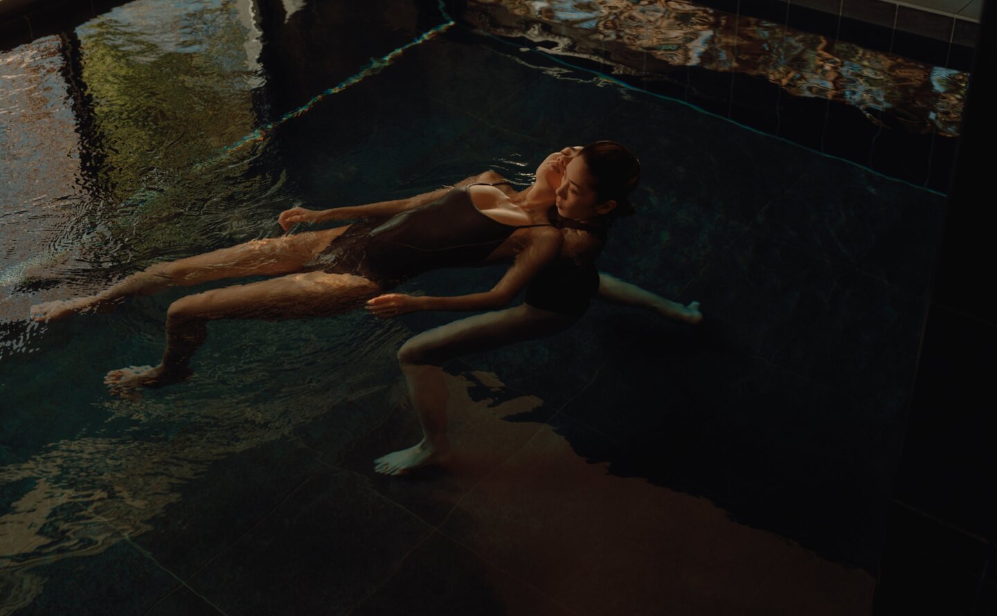 A woman floats peacefully in dark water during a Watsu wellness treatment at Amanemu, Japan.