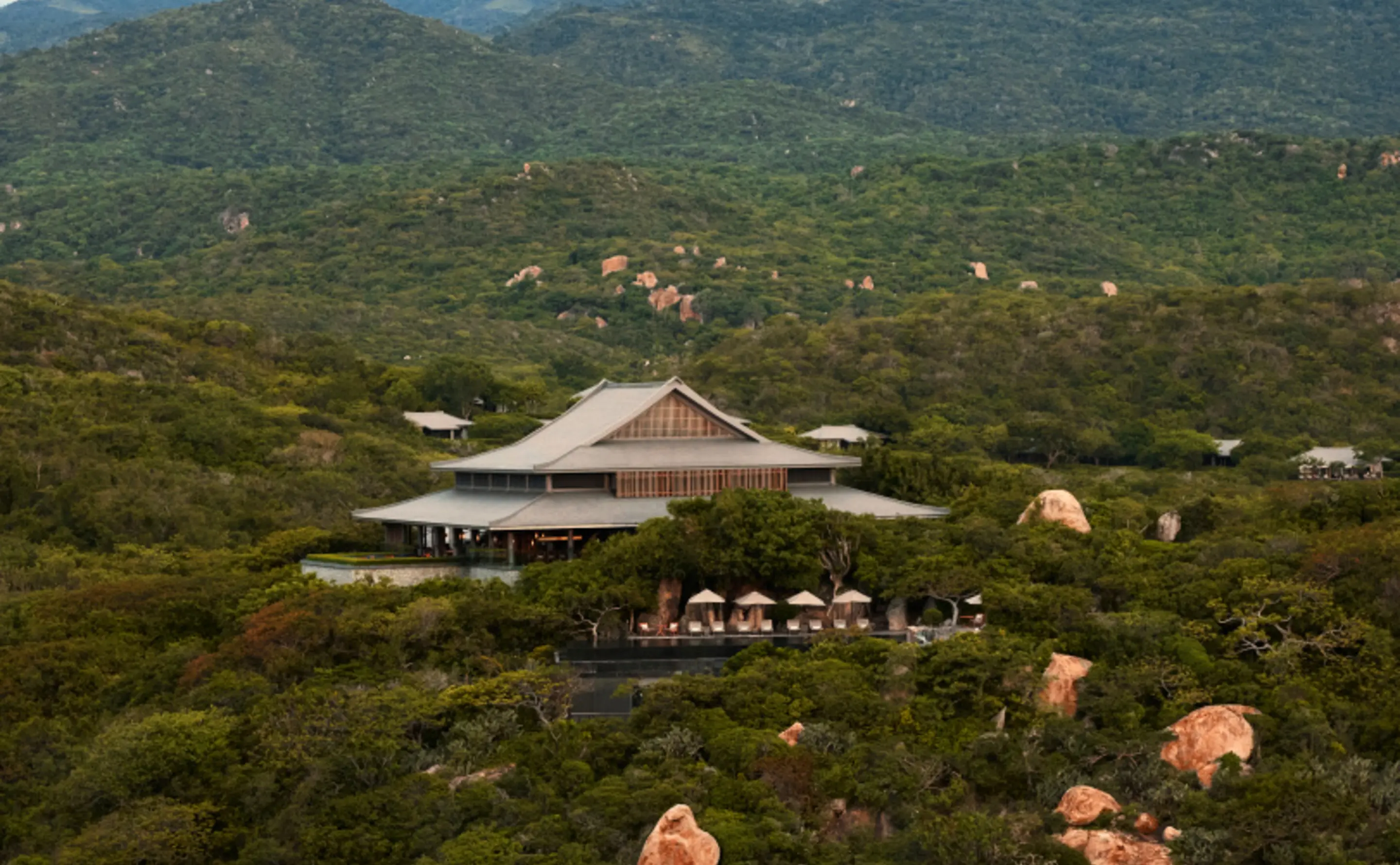 The Central Pavilion low in a fold of Nui Chua's forested hills, its double-tiered roof sweeping out over a colonnaded terrace and a row of white parasols, with pink granite boulders breaking through the green scrub on every ridge around it.