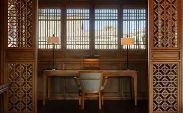 Carved wooden screens frame a desk and chair at Amandayan, with latticed windows overlooking distant mountains.