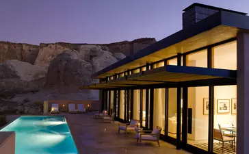 Amangiri's modern pavilion glows warmly at dusk, overlooking an illuminated plunge pool against desert rock formations.