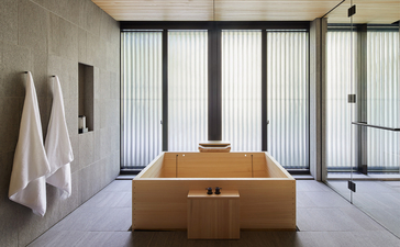 Wooden bathtub in a light-filled bathroom at Aman Kyoto, with vertical blinds and white towels.