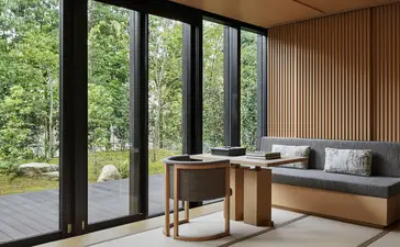 安缦京都度假村的景观框架，展示落地玻璃门通往绿色花园，室内设有木质书桌与座椅。