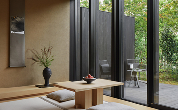 Spa relaxation area at Aman Kyoto with wooden seating, potted plant, and garden views through dark-framed doors.