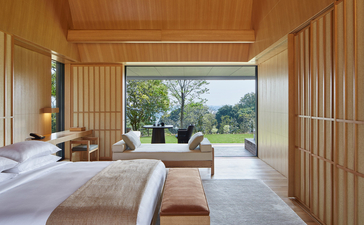 Principal bedroom at Amanemu with wooden interiors and views towards gardens and landscape beyond.