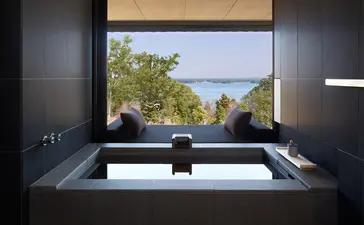 安缦伊沐度假村浴室内，深色浴缸面向窗户，远眺湖景和山峦。