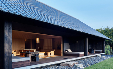 Amanemu resort's modern pavilion with dark timber facade and open-air living space at dusk.