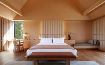 Principal bedroom at Amanemu with wooden platform bed, natural light and serene neutral palette.