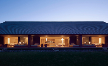 Amanemu resort's modern pavilion glows warmly at dusk against a clear sky.