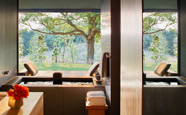 Amanemu guest seated by large windows overlooking serene landscape with water views.