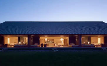 Amanemu resort's modern pavilion glows warmly at dusk against a twilight sky.