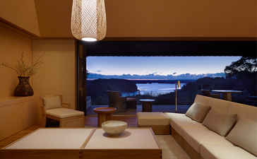 Principal bedroom at Amanemu with coastal views at dusk, featuring minimalist décor and large window framing the landscape.