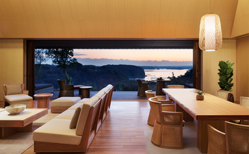 Amanemu principal bedroom with wooden furnishings overlooking coastal views through expansive windows.