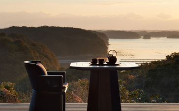 Woman standing at railing overlooking calm water and forested landscape at Amanemu.